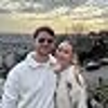 Two people smiling outdoors at sunset overlooking city